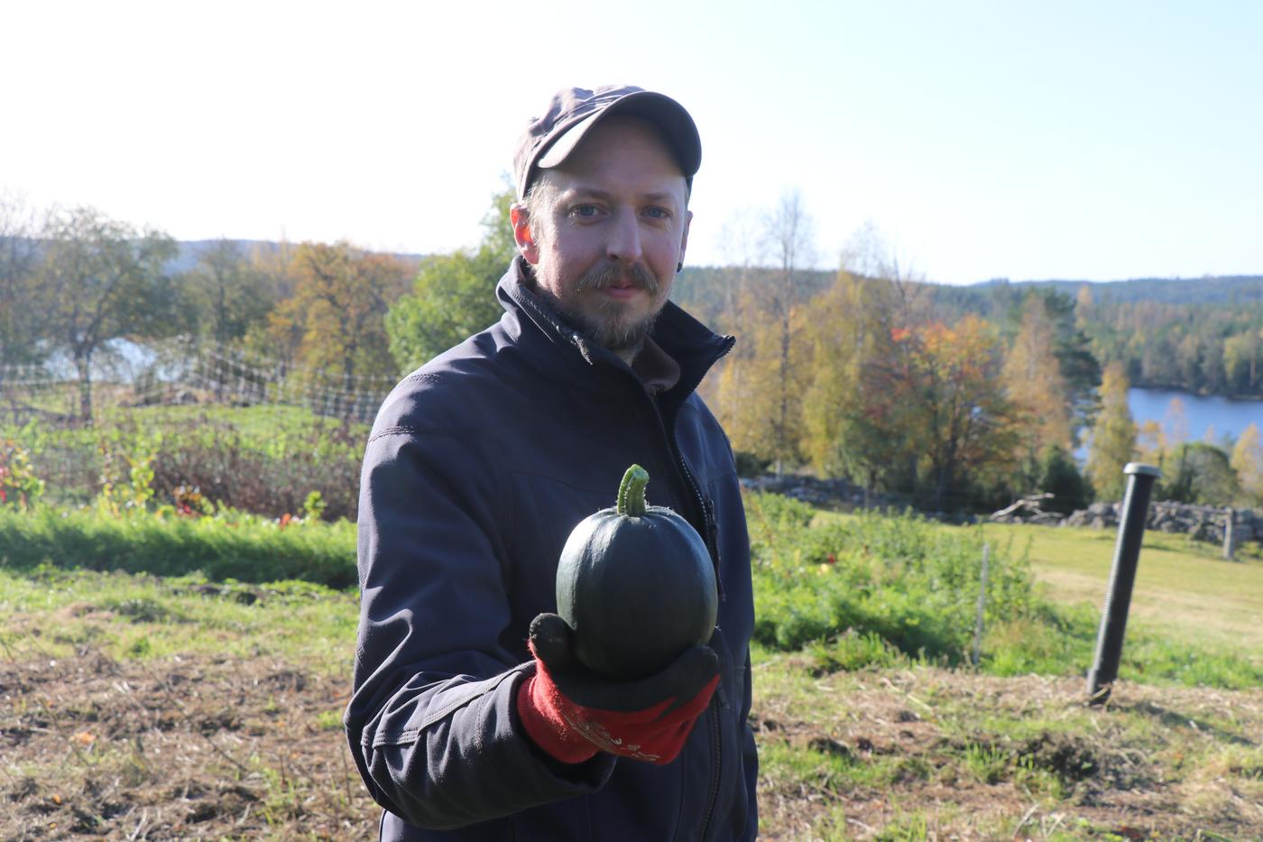 Mann med grønnsak i hånden med vott, landskap i bakgrunnen
