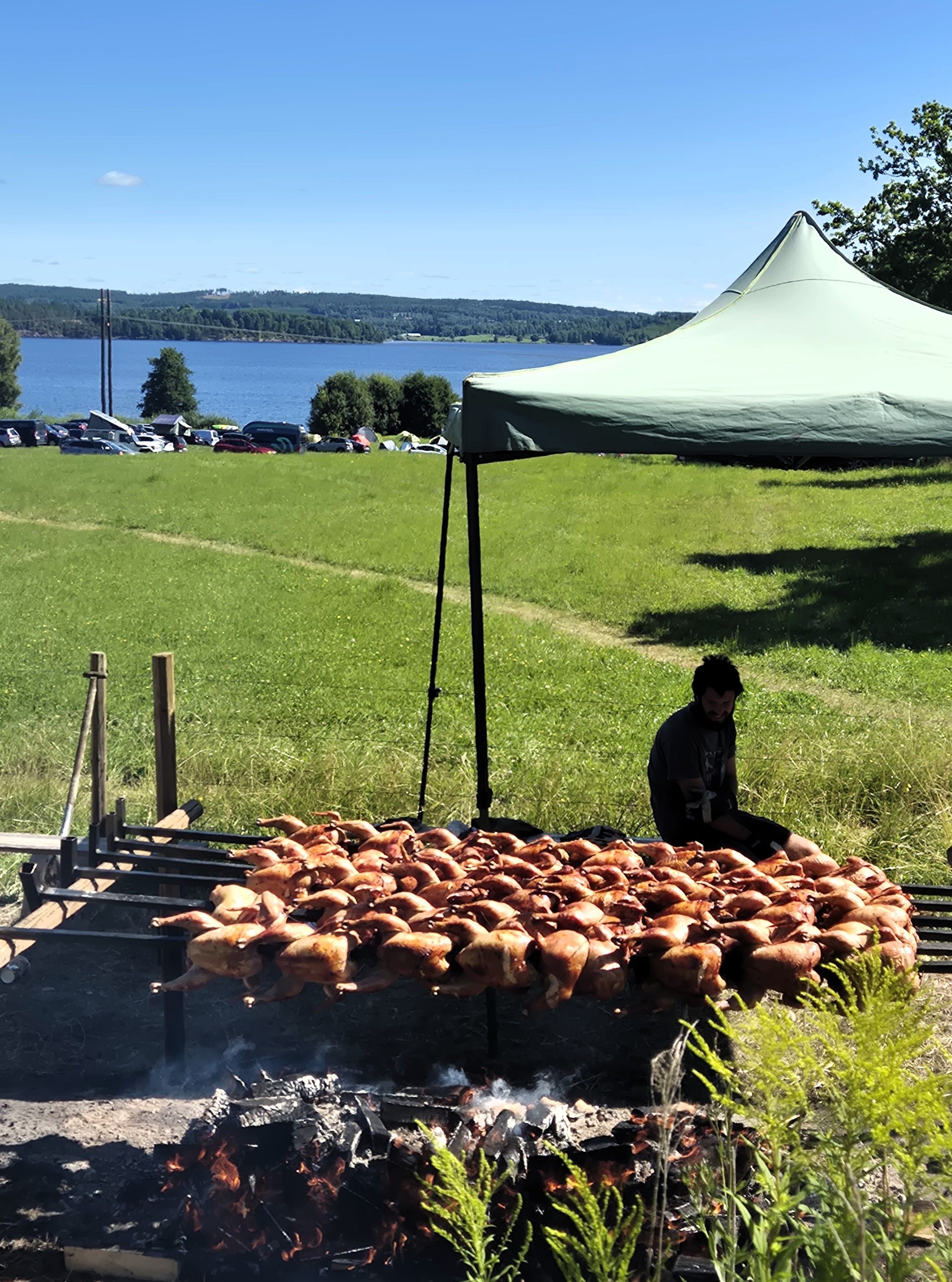 Person under et telt som griller kyllinger på lange spyd
