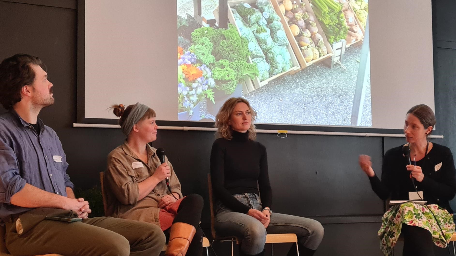 Fire mennesker som sitter på stoler foran en skjerm med et bilde av grønnsaker i kasser