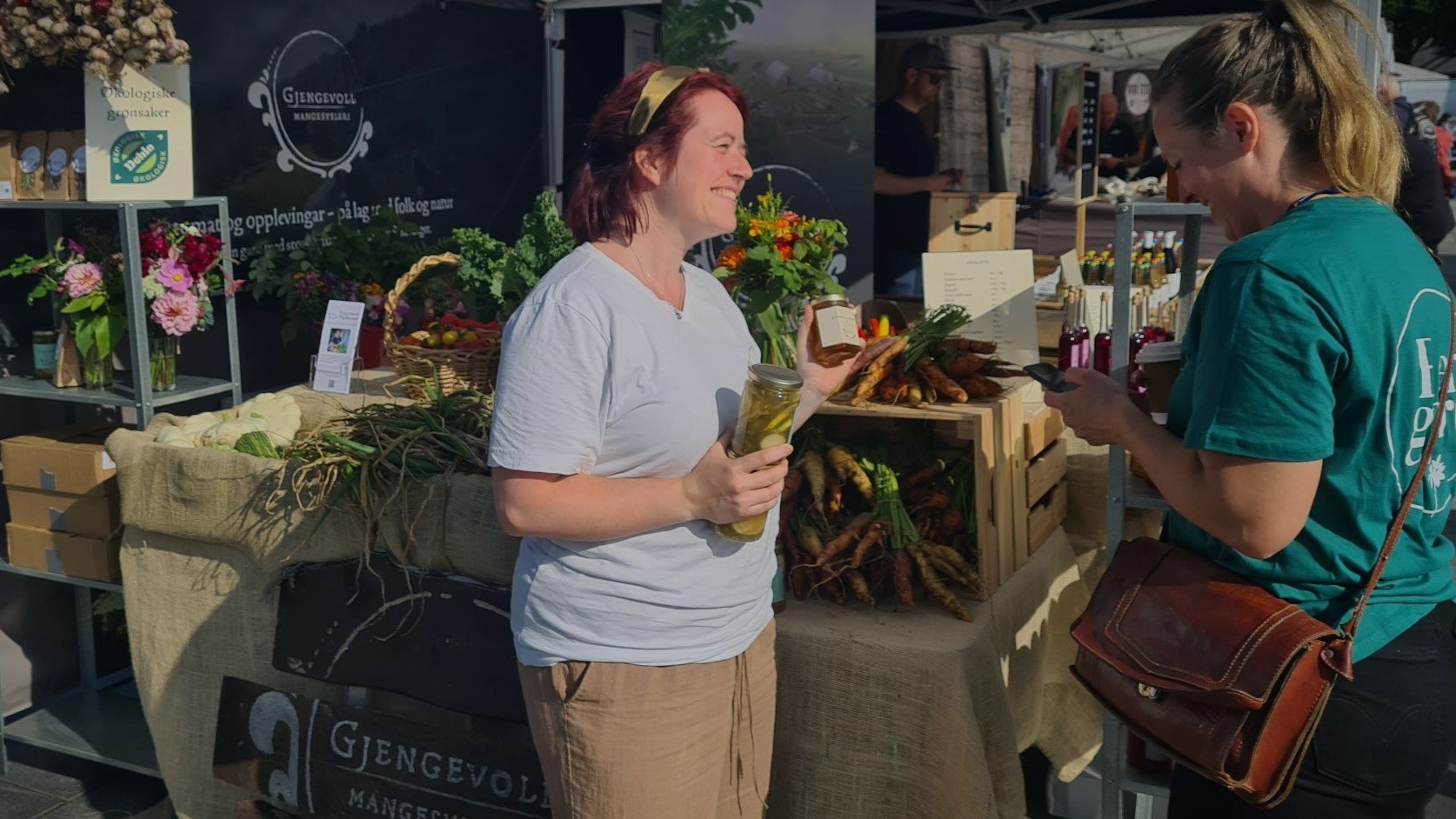 To kvinner som ser på matprodukter på flaske og i glass. Stand i bakgrunnen med grønnsaker.