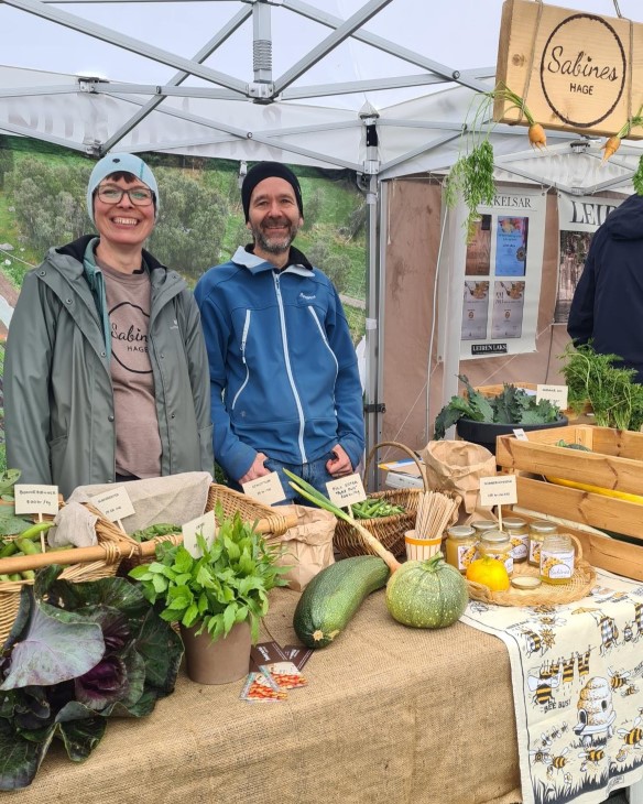 En Kvinner og en mann forran et bord med grønsaker. 

