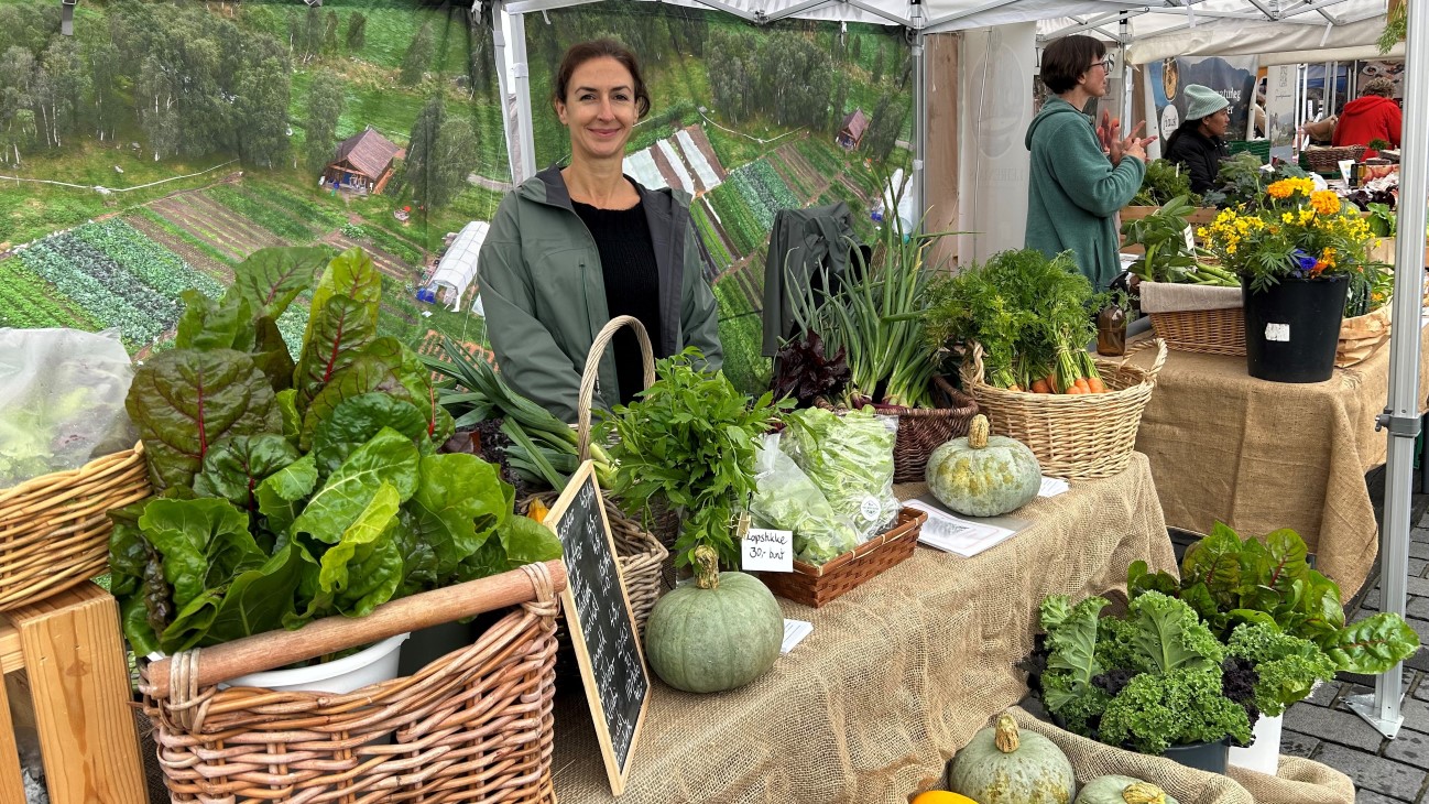 Kvinne med mye grønnsaker i en stand på et marked i Bergen.