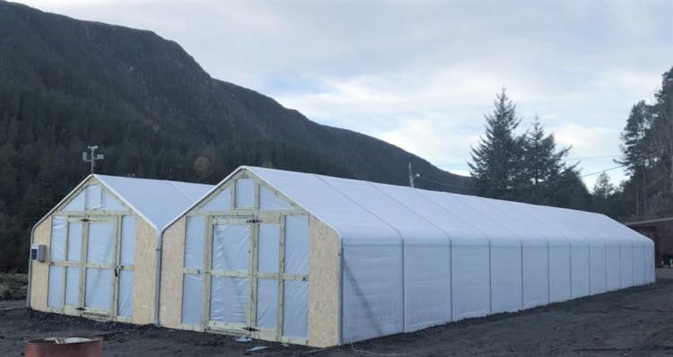 To tuneller i plast med treplater i endeveggene. Fjell i bakgrunnen. 