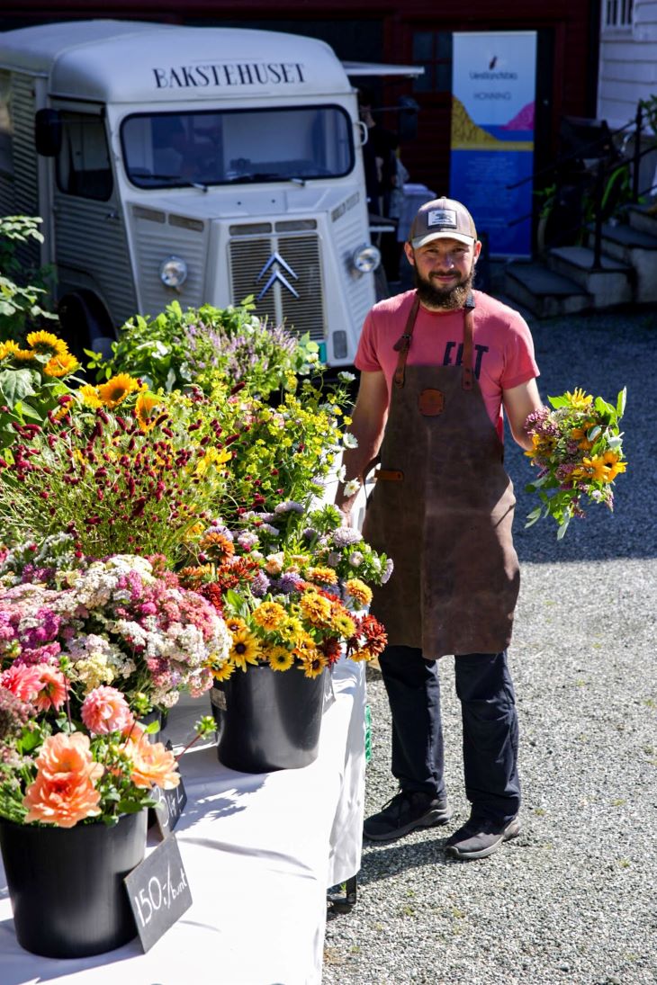 Mann med blomster i forgrunnen og en kassebil i bakgrunnen