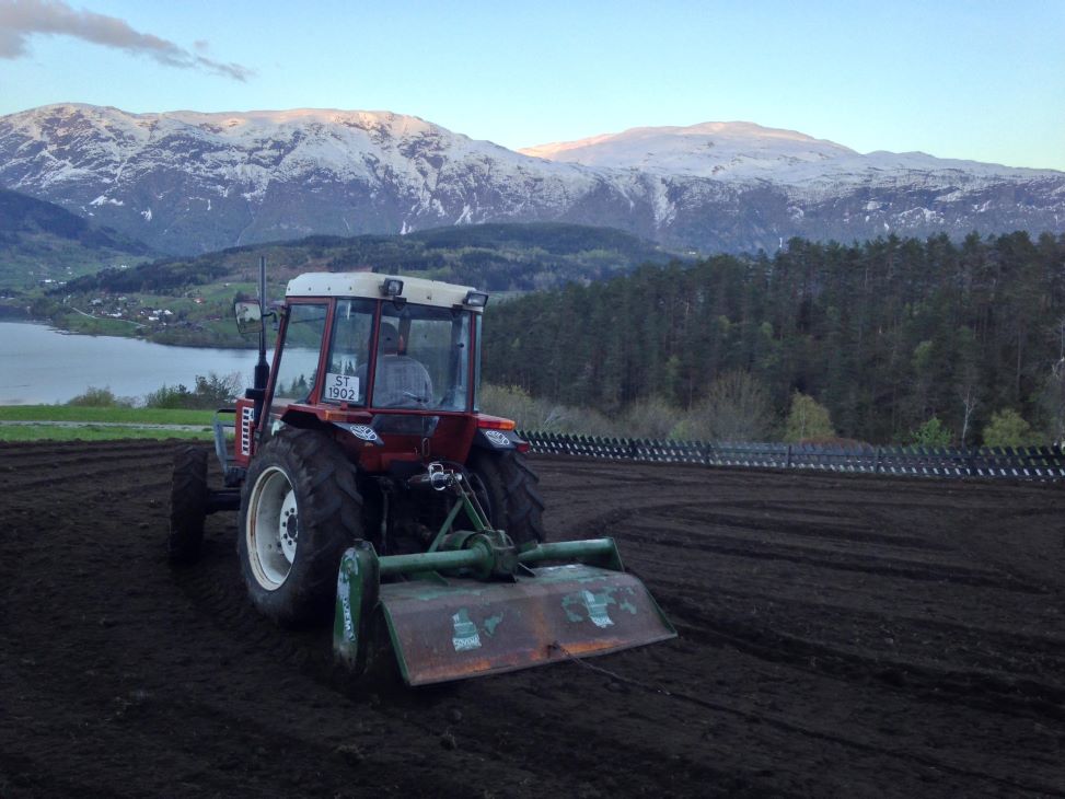 Traktor i åker med svart jord. fjell i bakgrunnen