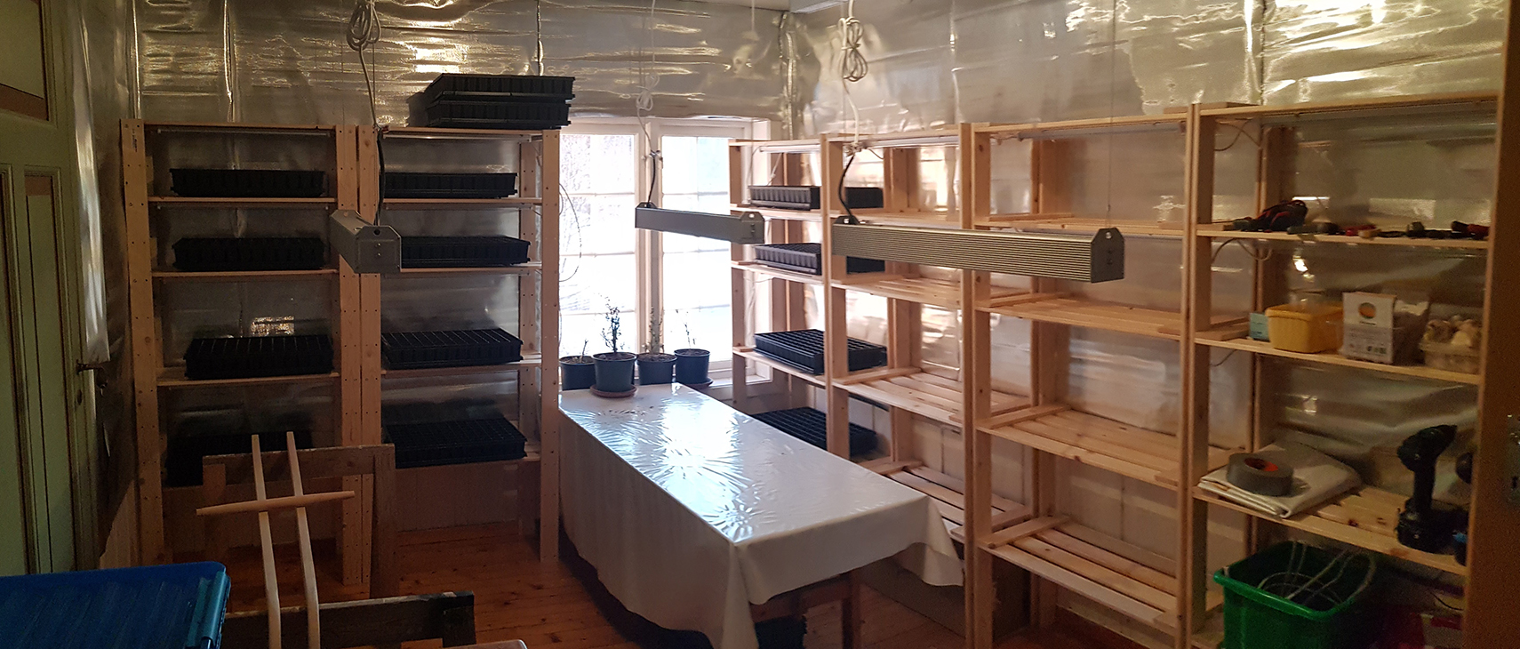 Et rom for oppal av planter, med et bord og hyller langs med sidene av rommet. 