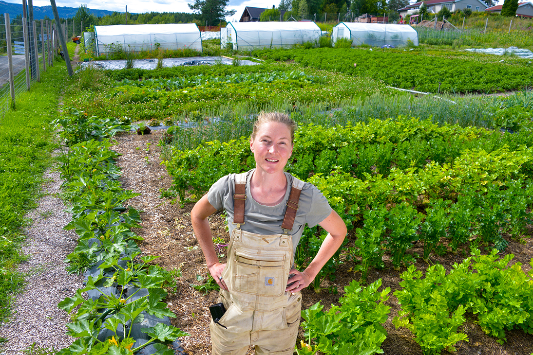 En kvinne forran et jorde med grønnsaksfelt. 