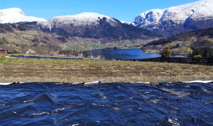 Siloplast i svart i forgrunnen, fjell med snø på i bakgrunnen